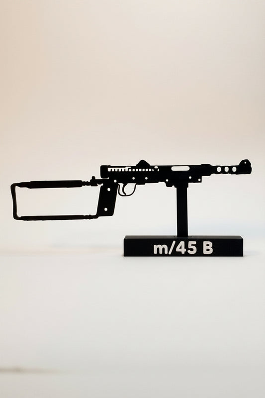 A black metal silhouette model of an m/45 B machine gun mounted on a black display base with white text, set against a plain off-white background.