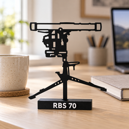 Lifestyle preview of the RBS 70 display model on a wooden home-office desk, with its labelled black base and recessed mounting slot.